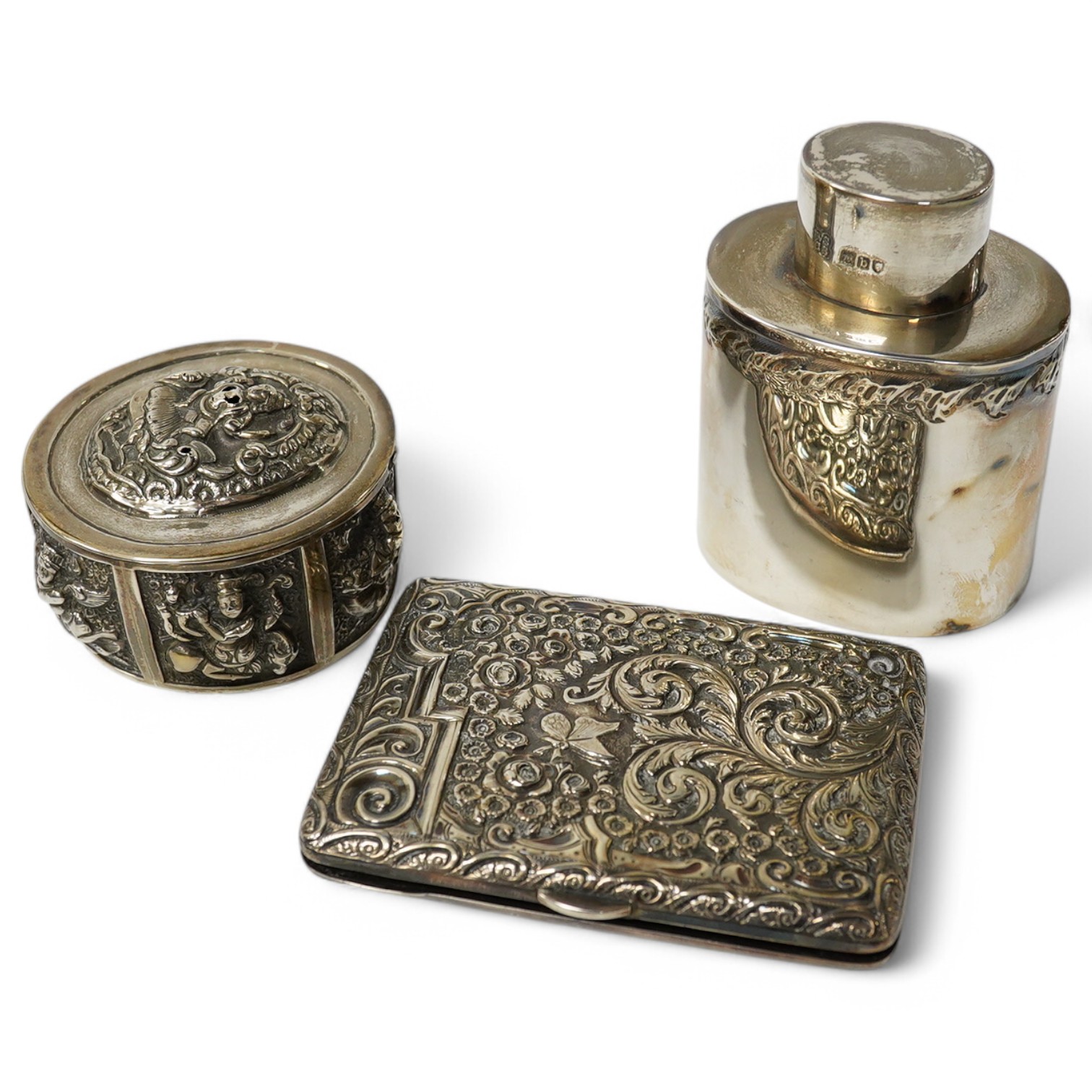 An Edwardian rectangular embossed silver mounted note case, leather lined, Goldsmiths & Silversmiths Co Ltd, London, 1901, 10.3cm, an oval silver tea caddy and cover and an Indian white metal circular box. Condition - po